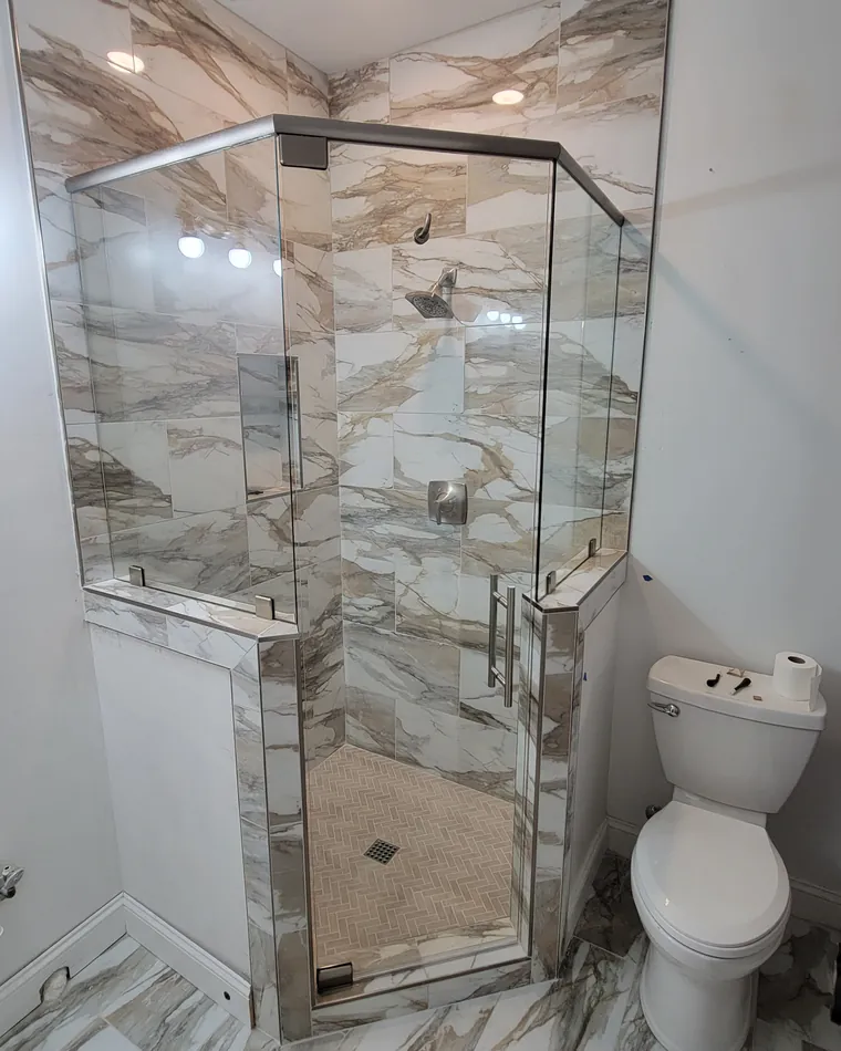 A neo-angle glass shower standing on two marble-tiled knee walls
